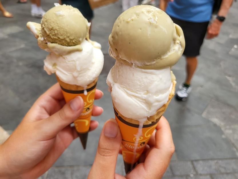 Two hands holding ice cream cones with green and white scoops.