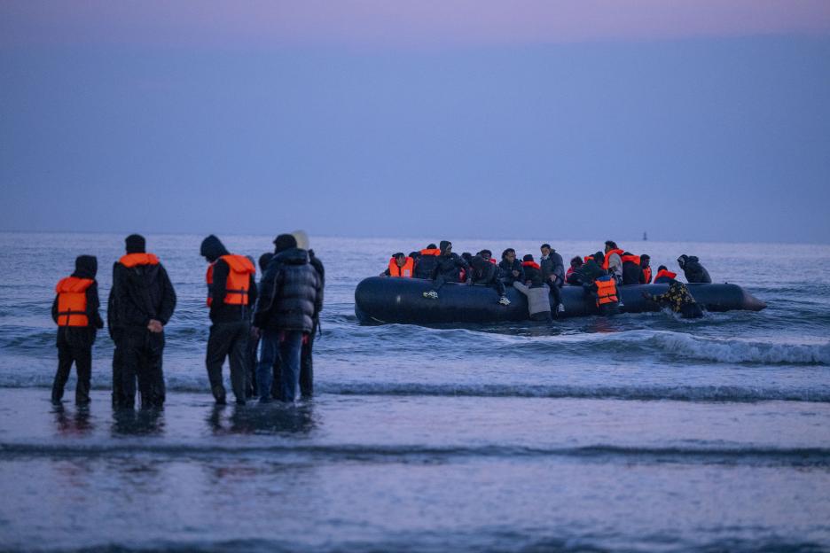 Migrants in an inflatable boat and standing in the water.