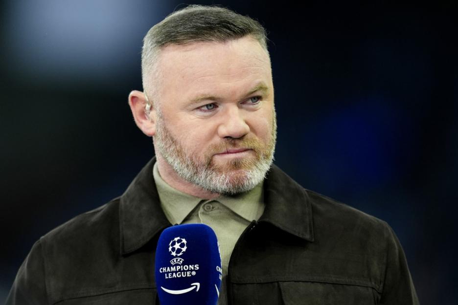 Wayne Rooney wearing a dark jacket and holding a microphone with the Champions League logo.