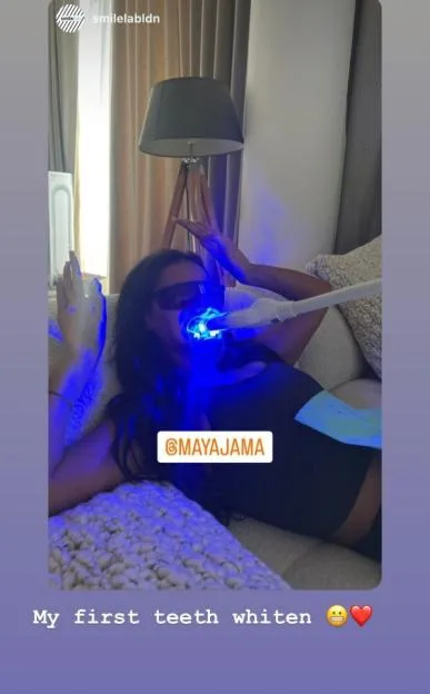 Maya Jama undergoing a teeth whitening treatment, wearing protective eyewear and a blue light device in her mouth.
