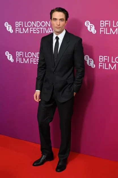 Robert Pattinson in a black suit, white shirt, and black tie on a red carpet in front of a BFI London Film Festival backdrop.