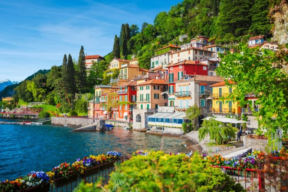 View of Varenna town on the shore of Lake Como in Italy, featuring colorful buildings nestled against a lush green hillside.