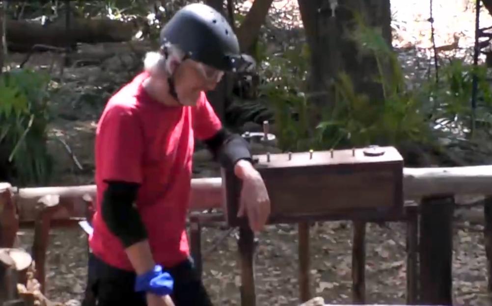 Jimmy Bullard in a red shirt, black helmet, and goggles, leaning on a wooden box with metal pins on top, on the set of 'I'm A Celebrity... Get Me Out Of Here! South Africa'.