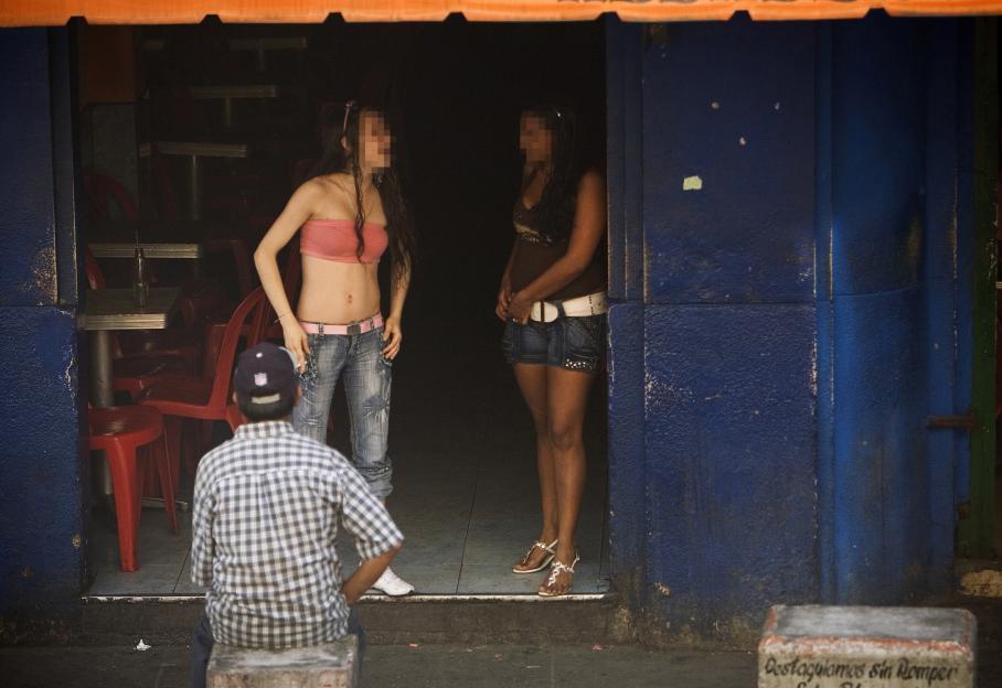 A man sits with his back to the camera, looking at two women standing in a doorway.