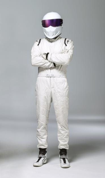 The Stig in a white racing suit with a white helmet and purple visor, arms crossed.