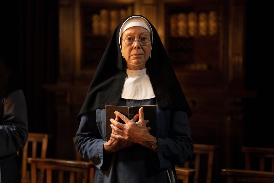 Jenny Agutter as Sister Julienne, a nun wearing a dark habit, holding a book.