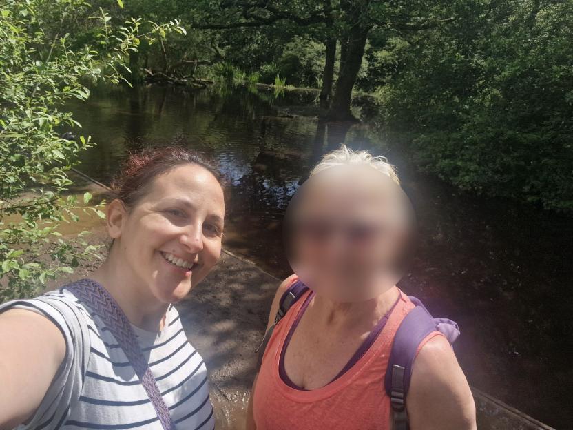 Annie Perez and a blurred-out friend in a wooded area with a body of water behind them.