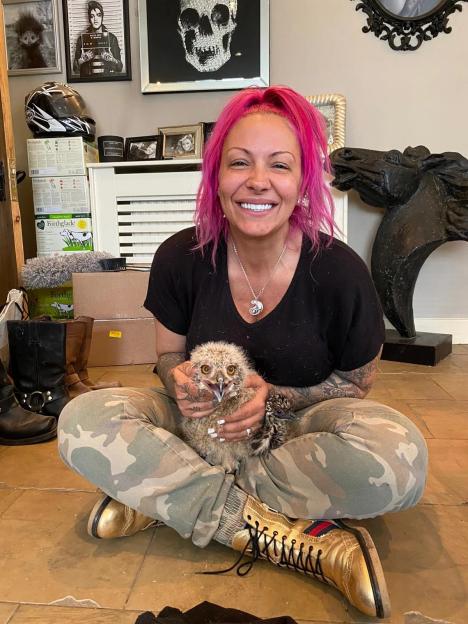 Jodie Marsh, with pink hair and a black shirt, holding a baby owl and another bird while sitting on the floor.