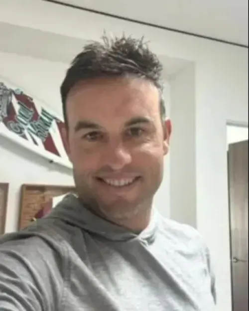 A man with spiky dark hair and a gray hoodie smiles at the camera.