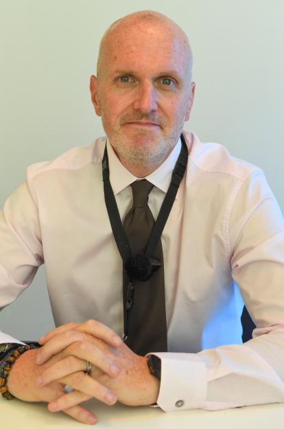 Det. Sgt. Richard McCorry wearing a light pink shirt and dark tie, looking at the camera.