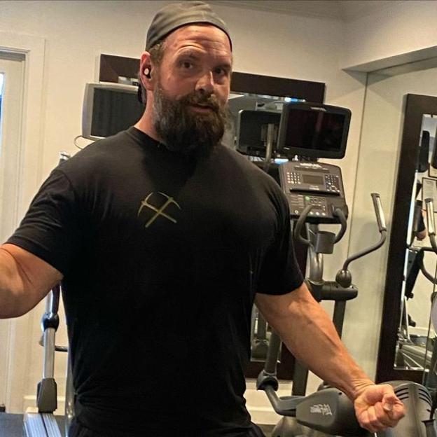 Ethan Suplee, wearing a black shirt and cap, looks muscular while exercising in a gym.