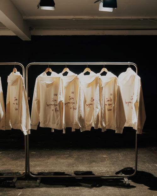 White hooded sweatshirts with red writing hanging on a clothing rack.
