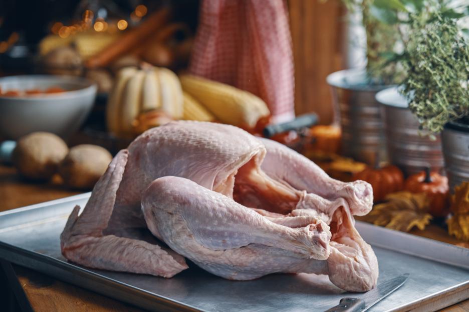 Raw turkey on a tray with vegetables and ingredients in the background.