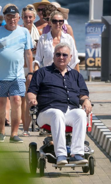 Eamonn Holmes in a motorized wheelchair with Katie Alexander and other people on holiday in Cyprus.