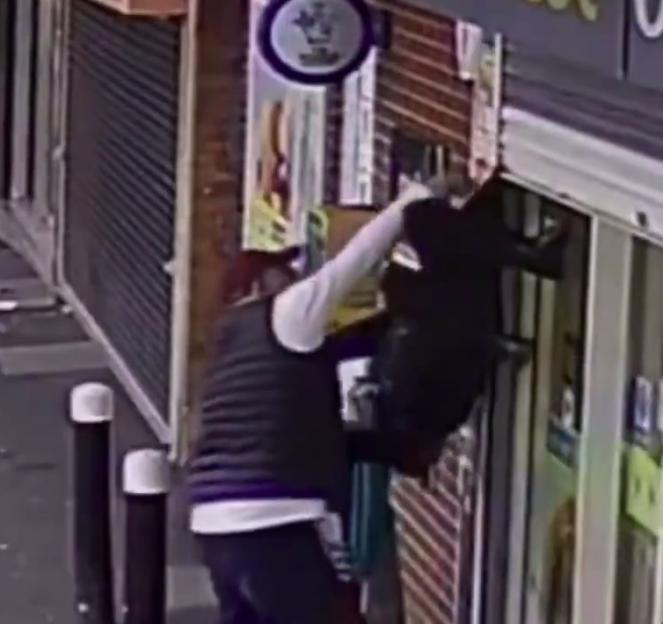 An elderly woman caught by her coat, hanging upside down from a metal security shutter at a convenience store.