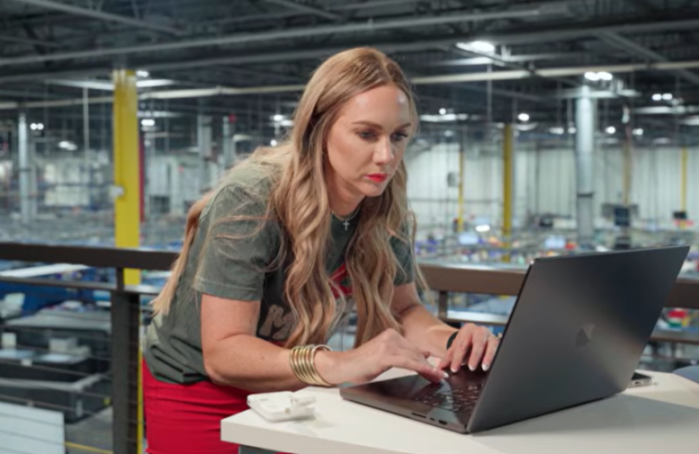 A woman in a warehouse setting uses a laptop.