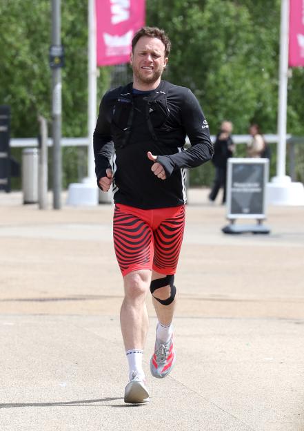 Olly Murs running with red and black patterned shorts and a black long-sleeved shirt with a black chest harness.
