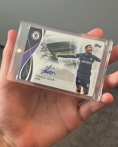 Hand holding a encased Thiago Silva "Lineage 120" Topps football card with his autograph and a Chelsea FC logo.