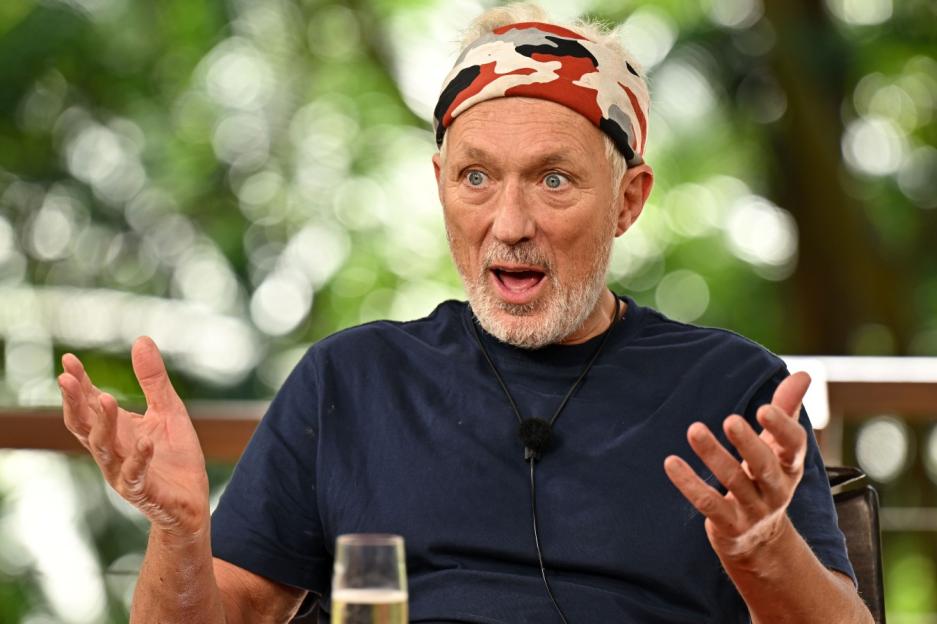 A man with a camouflage headband and blue shirt speaks animatedly, gesturing with both hands.