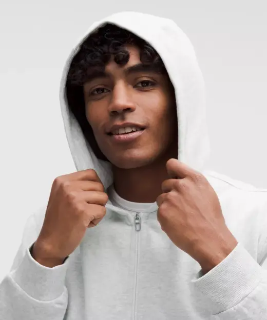 Man with curly hair wearing a light gray zip-up hoodie.