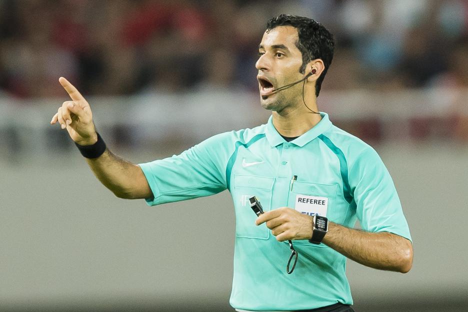 Referee Abdulrahman Al-Jassim gesturing and holding a whistle during a soccer match.