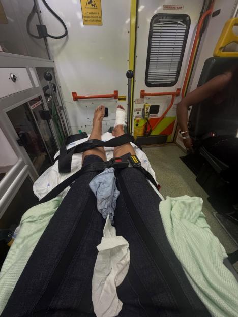 Person lying on a stretcher with one foot bandaged, inside an ambulance.