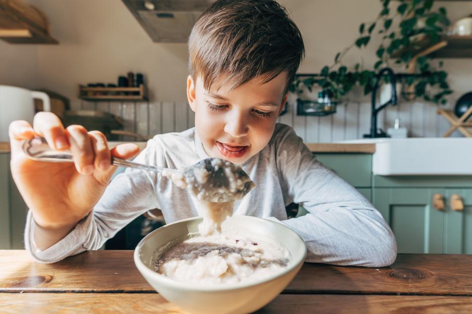 A boy eating porridge from a bowl with a spoon.