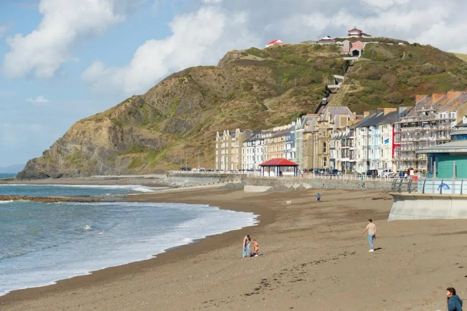 Aberystwyth seafront with sandy beach, promenade buildings, and Constitution Hill in the background.