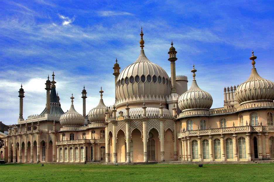The Royal Pavilion in Brighton, East Sussex, a 19th-century palace with Indian architectural influences, featuring multiple domes, minarets, and ornate detailing under a blue sky.