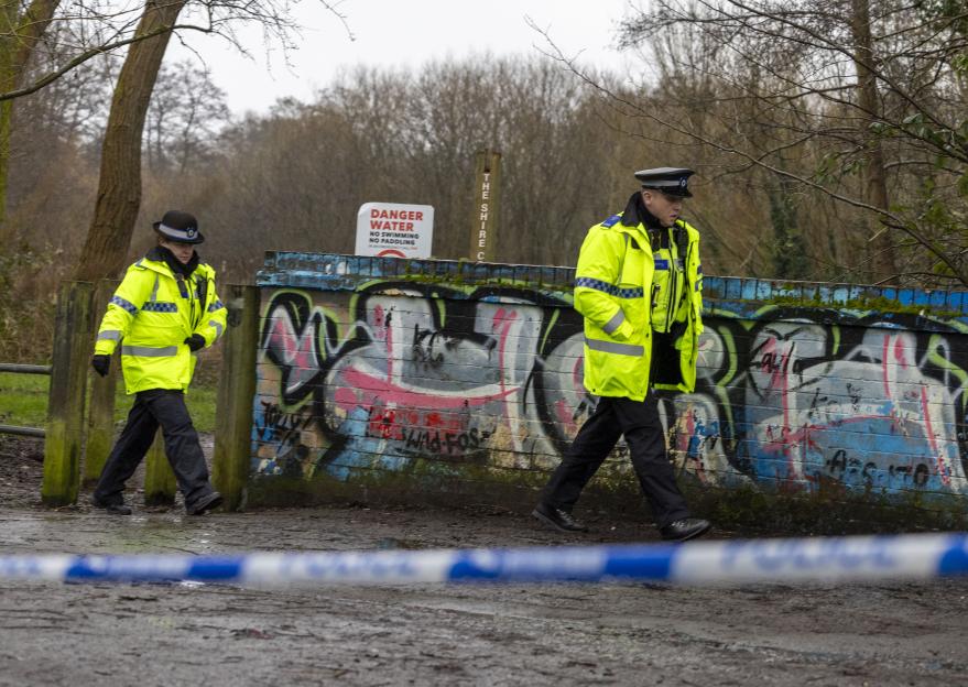 Two police officers in high-visibility jackets walk past a graffiti-covered wall at Shire Country Park.
