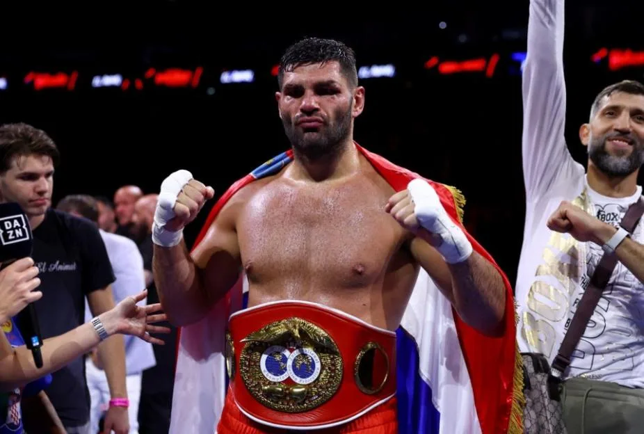 Boxer Filip Hrgovic with his IBF world heavyweight title belt and a flag draped over his shoulders.