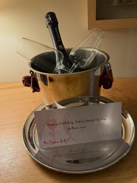 Champagne bottle in an ice bucket with two glasses and a birthday card addressed to India.