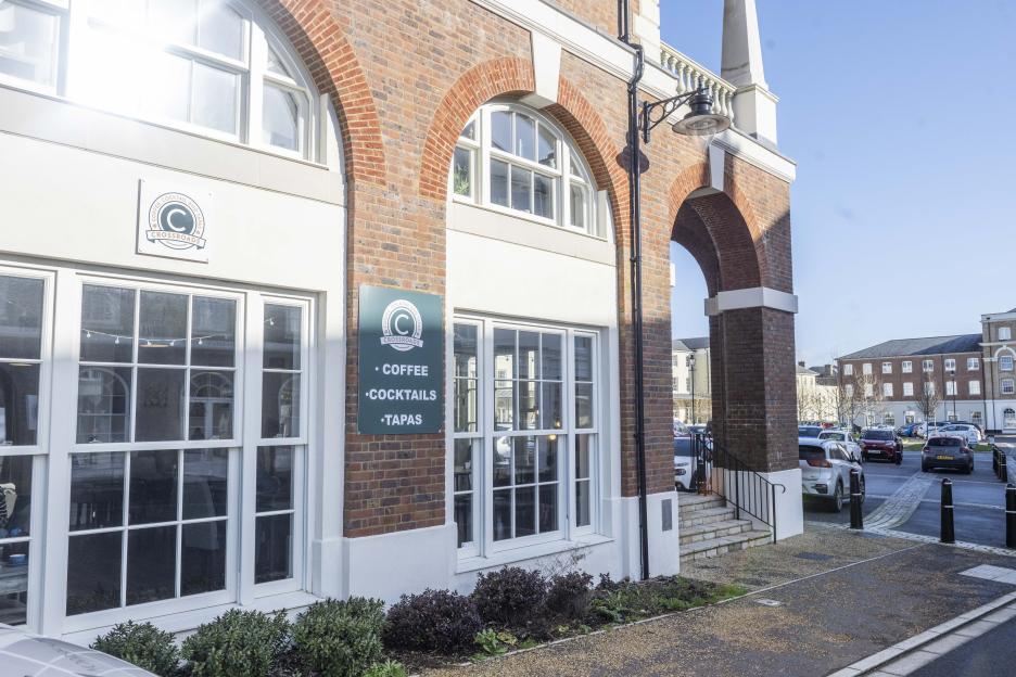 The exterior of Crossroads cafe, a brick building with white window frames and a sign listing "Coffee, Cocktails, Tapas".