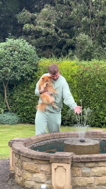Tom Clare holding a Pomeranian while touching a fountain.