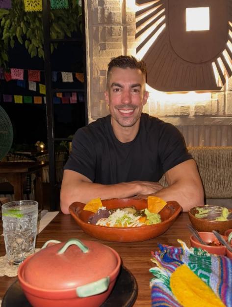 Filip Gregov smiles at a table with food and a drink in front of him.