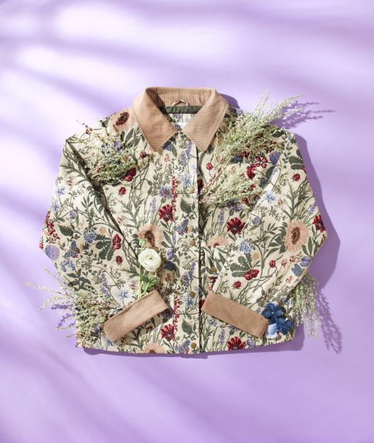 A beige floral jacket with a light brown corduroy collar and cuffs on a purple background, surrounded by white flowers.