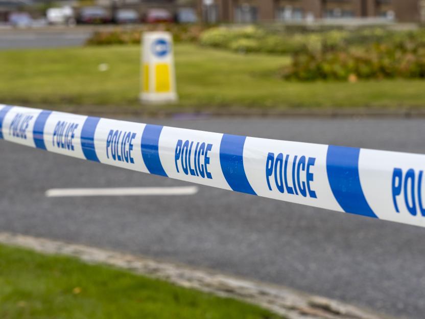 Police tape with "POLICE" written on it in blue, cordoning off a road.