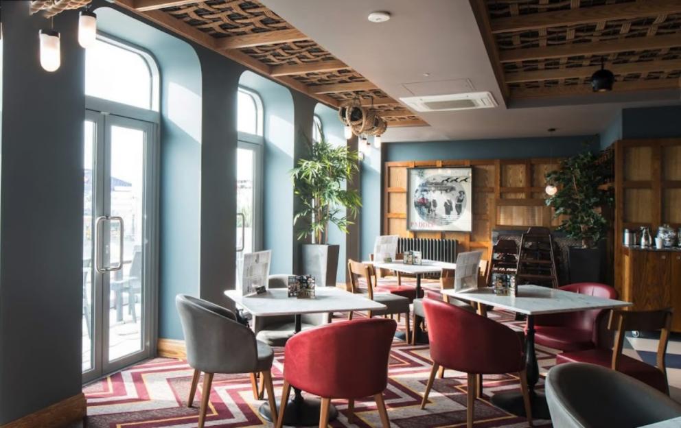 Interior of a modern restaurant with red and gray chairs, marble-topped tables, and large windows.