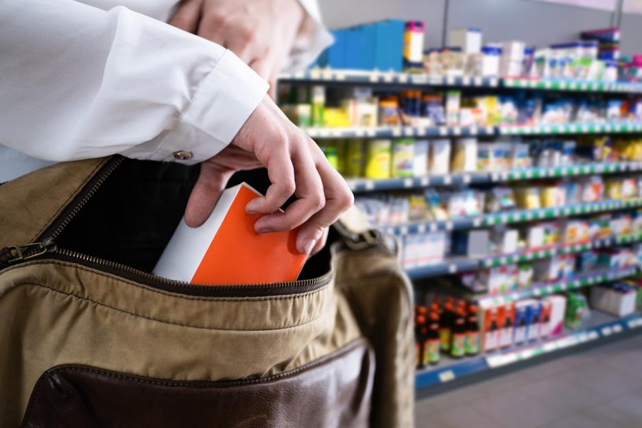 A person's hands placing a red and white box into a bag, with supermarket shelves visible in the blurred background.
