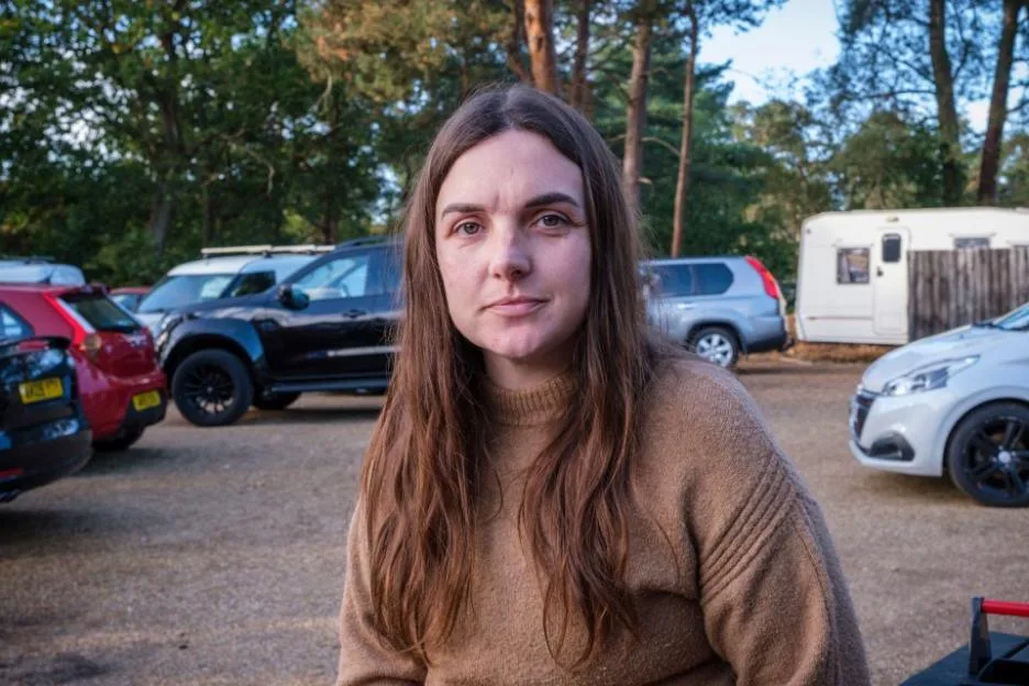 Businesswoman Steph Donaldson stands in a gravel lot with cars and a trailer behind her.