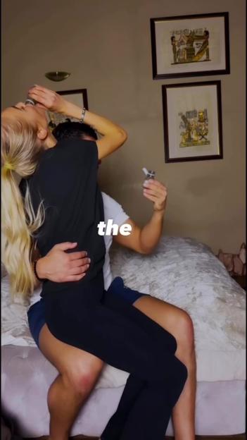 A blonde woman sitting on a man's lap, drinking from a small bottle while the man holds a spray bottle.