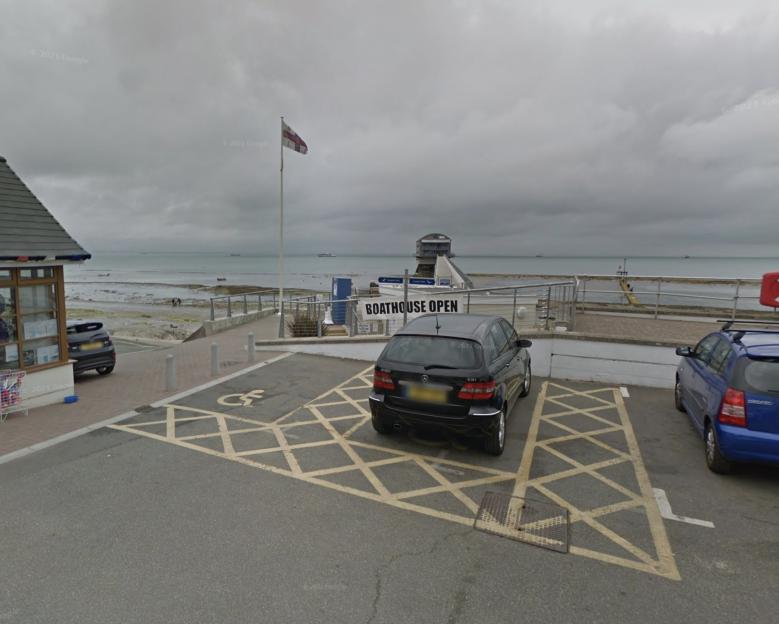 A car park at Bembridge Beach with a boathouse and cloudy sky in the background.