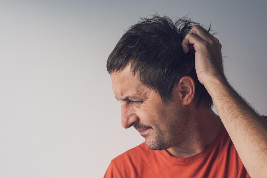 Man in an orange shirt scratching his head, looking frustrated and confused.