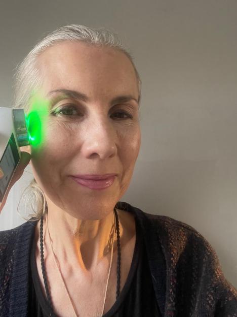 Katrina Verdon-Roe using an Optra machine with a green light on her face.