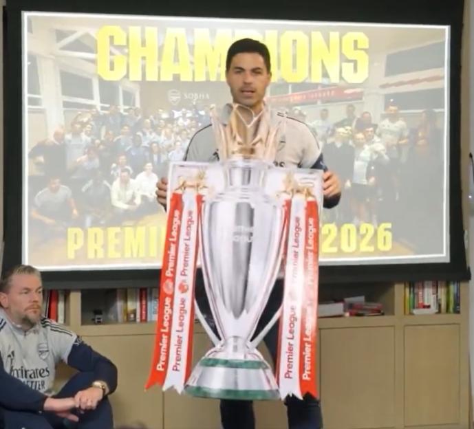 Mikel Arteta holding up a cardboard cutout of the Premier League trophy.