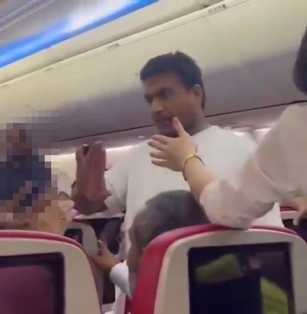 A man in a white shirt being restrained on an airplane by a woman.