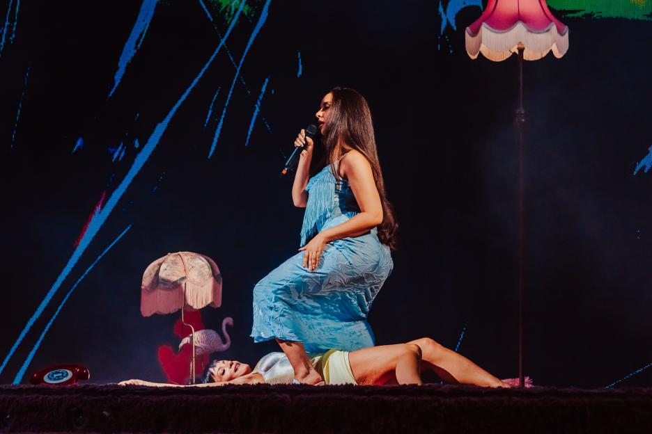 Lily Allen kneels over Jade Thirlwall, who is lying on her back, during a performance.