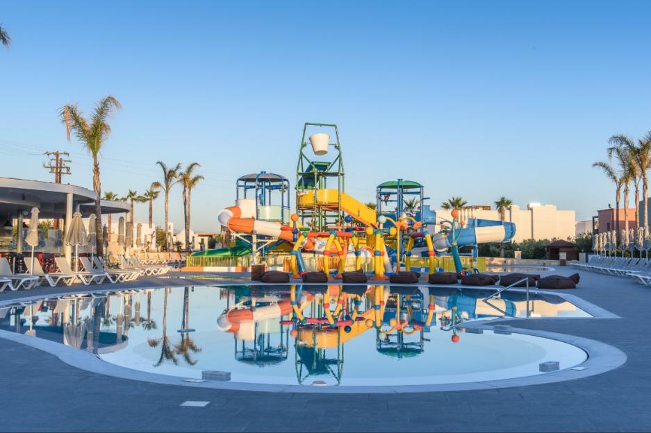 A resort pool with water slides and palm trees, with lounge chairs and umbrellas in the background.