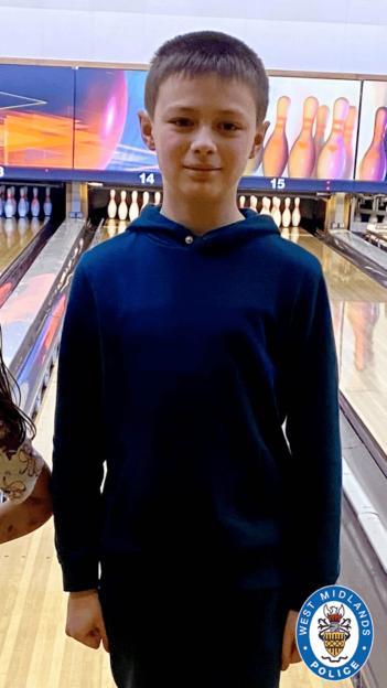 Leo Ross, 12, smiling and standing in a bowling alley in front of pins and screens.