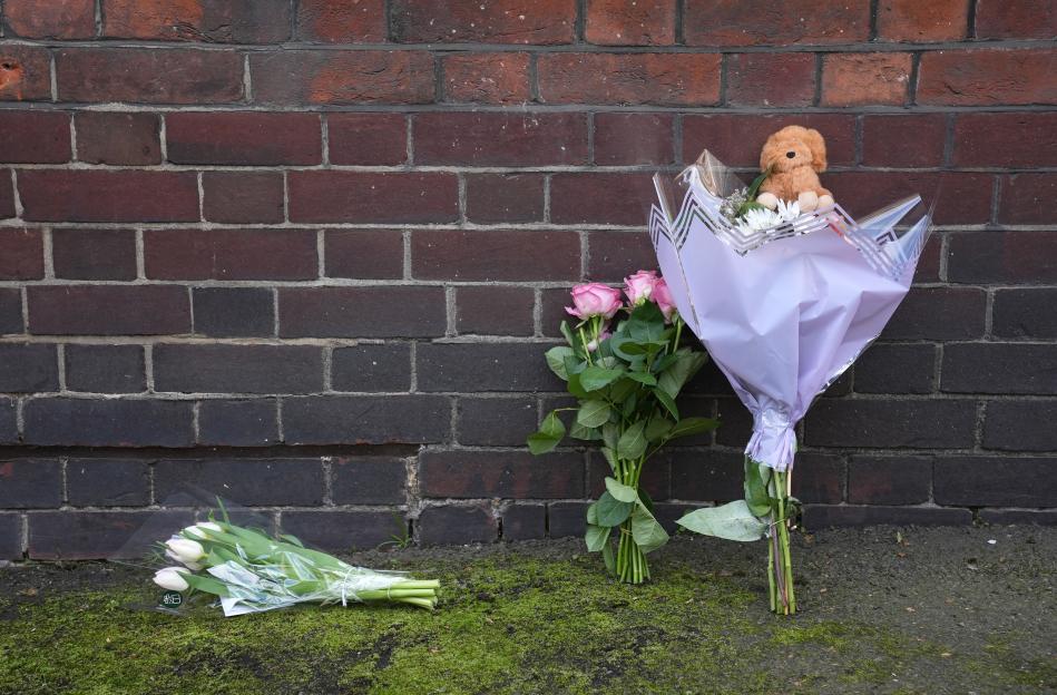 Flowers and a teddy bear left near a building after a baby girl's death.